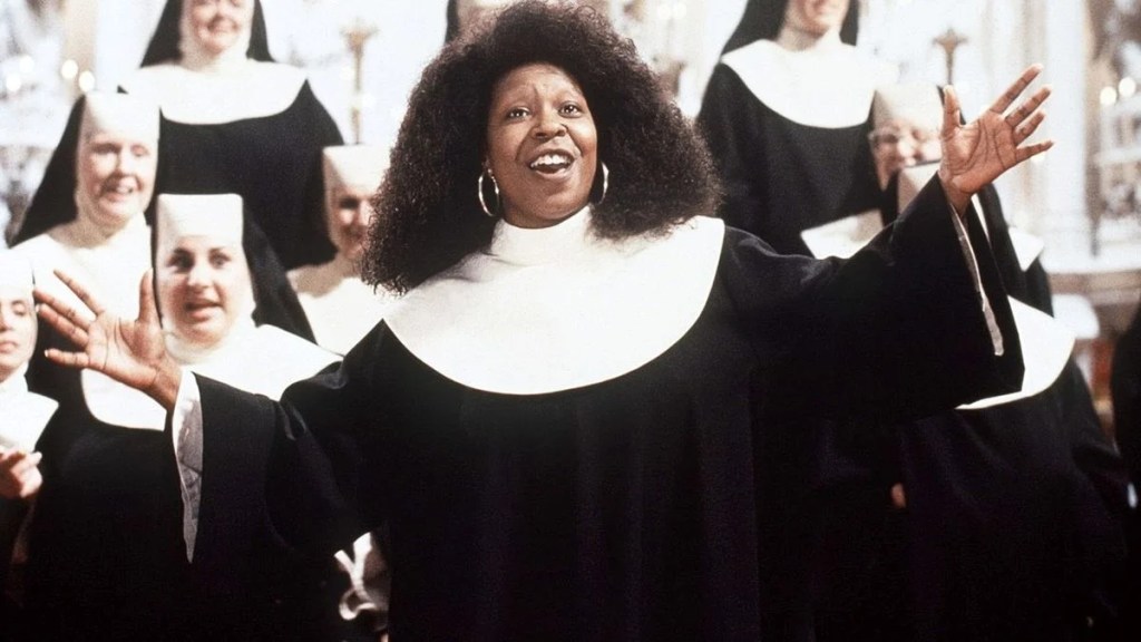 Whoopi Goldberg, dressed in a nun’s habit, stands joyfully with arms outstretched in front of a group of singing nuns in a church setting. The image is from the film Sister Act, capturing a lively choir scene filled with energy and celebration.