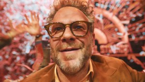 Seth Rogen as Matt Remick in "The Studio," smiling in front of red lights in the background